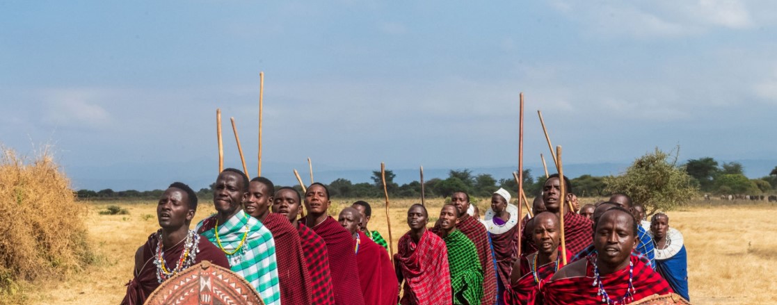 Maasai warrior in traditional attire standing against a backdrop of the African savannah