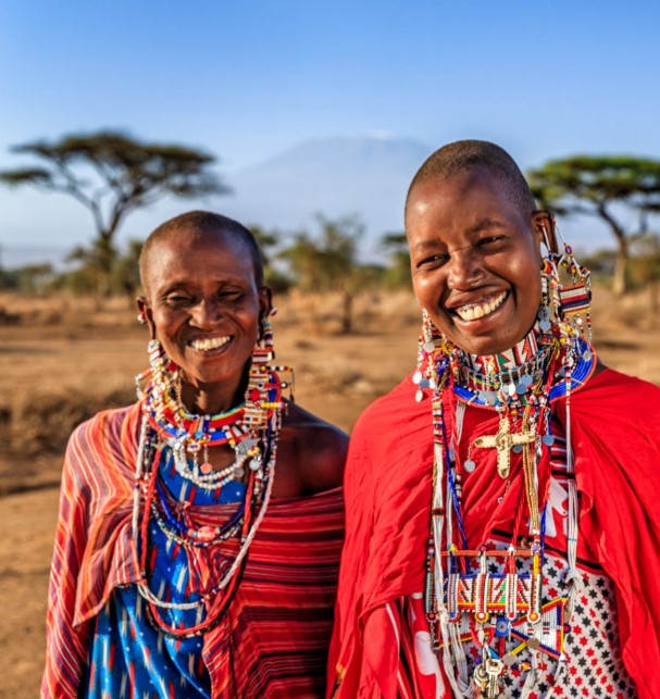 Traditional Maasai woman wearing colorful beaded jewelry and red shÃºkÃ , standing in an open savanna landscape.