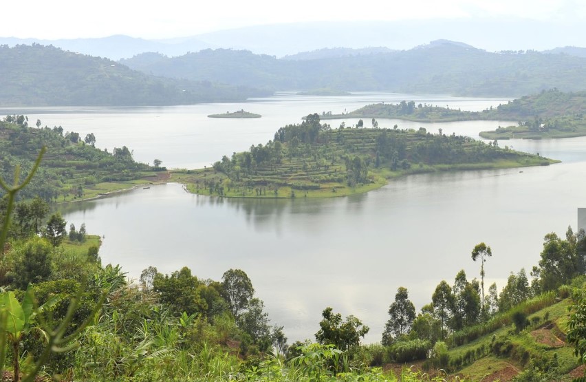A serene view of Rwanda's lakes with calm water, lush green hills, and a colorful sunset reflecting on the surface